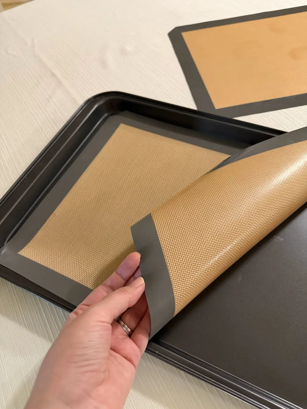 Lámina de silicona de color beige con borde gris colocada sobre una bandeja metálica de hornear.